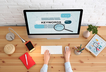Woman searching keywords with computer at wooden table, top view