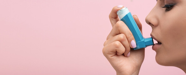 Young woman using asthma inhaler on pink background, space for text. Banner design