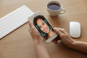 African-American woman using smartphone with facial recognition system at table, closeup. Biometric...