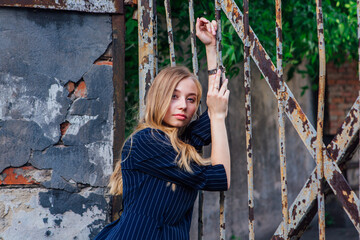 Close up portrait of a fashion look's woman near the old rusty gate. Young woman modern portrait.