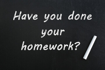 Piece of chalk and phrase HAVE YOU DONE YOUR HOMEWORK? on blackboard, top view