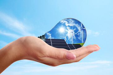 Alternative energy source. Woman holding light bulb with solar panels and wind turbines, closeup