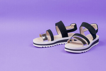 Stylish summer black women's sandals on a lilac background.