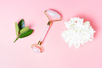 Face roller with green leaves on pink background, concept of facial massage, copy space