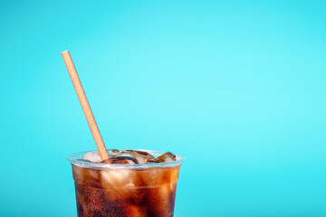Coffee with ice in a plastic glass with a tube on blue background, a copy of the space