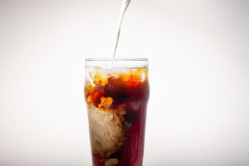In a glass of coffee poured milk on white background, the view from the front