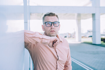 Businessman in a pink shirt stands against the backdrop of a modern building.
