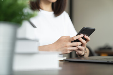 Young woman hand holding smartphone and chatting with friends at social network on the table.