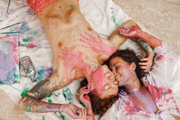 Portrait of a pair of lovers painted in bright colors, hugs and smiling, while lie on the floor at...