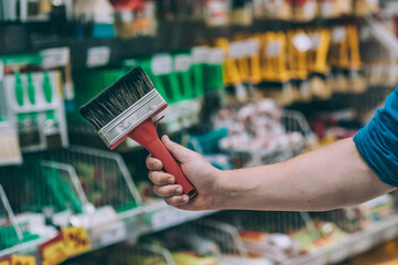 A buyer in a hardware store selects a product. A man holds a paint brush in his hand.