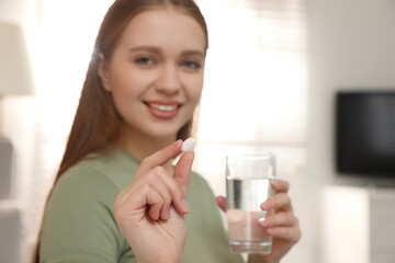 Woman with glass of water and vitamin pill indoors, focus on hand