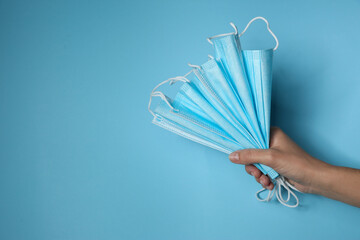 Woman holding disposable face masks on light blue background, closeup with space for text....