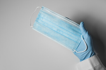 Doctor in latex gloves holding disposable face mask on light background, closeup with space for text. Protective measures during coronavirus quarantine