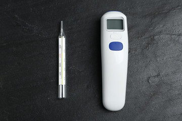 Non-contact infrared and mercury thermometers on black slate background, flat lay
