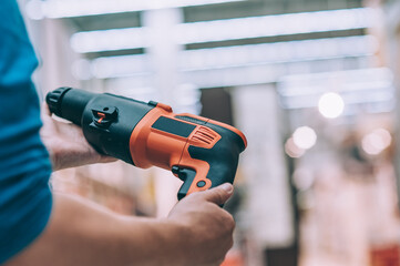 A man holds an electric drill in his hand for drilling. A buyer in a hardware store selects a...