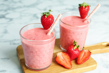 Tasty strawberry smoothies in glasses on wooden board