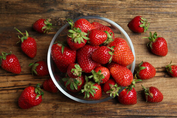 Delicious ripe strawberries in glass bowl on wooden table, flat lay