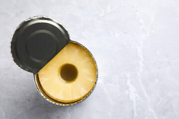 Open tin with canned pineapple on light grey marble table, top view. Space for text