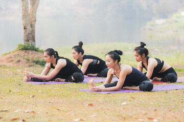 Group of asian women doing yoga beside the lake in outdoor park.