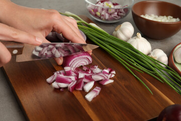 Fototapeta na wymiar Woman cutting red onion on wooden board, closeup