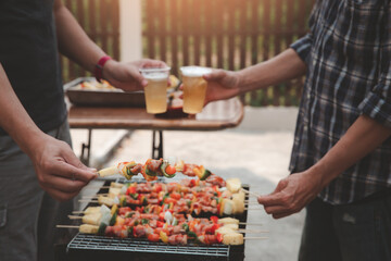 Young men cheers for a drink at a BBQ party between friends. Food, drink, people and family time concept.