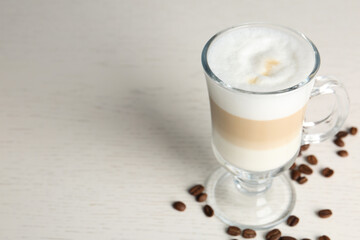 Delicious latte macchiato and coffee beans on white table, space for text