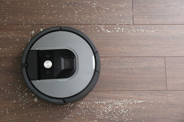 Modern robotic vacuum cleaner removing scattered rice from wooden floor, top view. Space for text