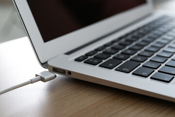 Modern laptop and charging cable on wooden table, closeup