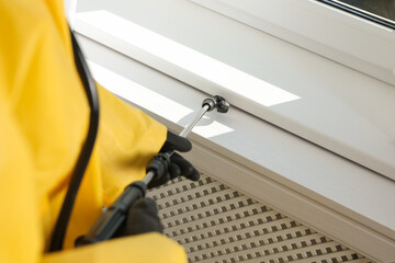 Pest control worker spraying pesticide on window sill indoors, closeup