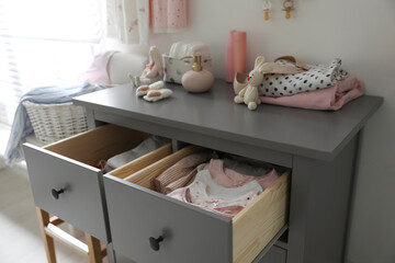 Open cabinet drawers with baby clothes in child room