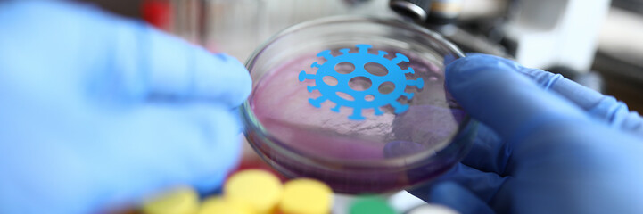 Male chemist hand in blue protective gloves hold petri dish closeup background. Medical lab research antivirus concept