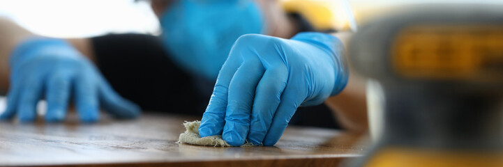Carpenter in gloves cleans polishes wooden surface. Joiner polish wooden surface canvas on table. Properties wood different species. Carpenter understands wood species and knows how to process