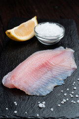 White fish boneless fillet on dark background with sea salt around, close up, fresh pangasius fillet