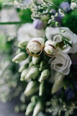 Close up of golden rings, hanging on flower buds of wedding bouquet, white tea roses