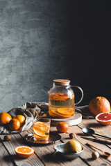 Citrus tea in a transparent teapot on a table with grapefruit and on a wooden table. Healthy drink.