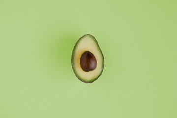 photo of half an avocado on a soft green background with  yellow and green flesh and a brown stone
