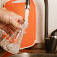 A man pours tap water into a glass flask.