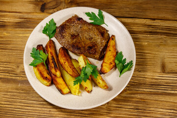 Fried beef steak with potato wedges on wooden table. Top view