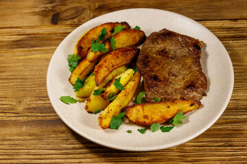 Fried beef steak with potato wedges on wooden table
