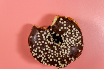 Bitten tasty chocolate donut on a pink background. Top view