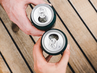 Two can of beer, female and male hands on the background of a beautiful, wooden surface. Directly...
