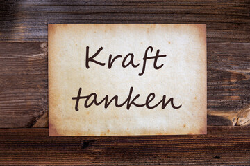 Obraz premium Old Grungy Paper With German Text Kraft Tanken Means Relax. Wooden Background