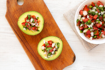 Homemade Pico de Gallo Stuffed Avocado on a rustic wooden board on a white wooden surface, top view. Flat lay, overhead, from above.
