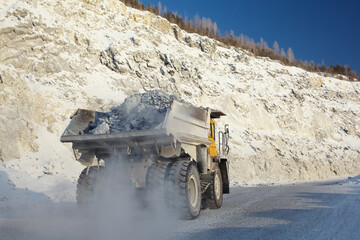 Heavy mining dump truck transports ore stone in the quarry mining enterprise, close-up. Mining industry.