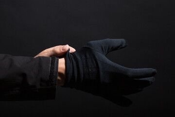 Hand in black gloves of a crime on a black background. Gloves are worn on the hand. The man puts a...