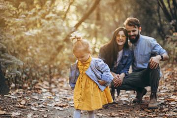 Naklejka na ściany i meble happy young family: stylish father, beautiful mom and sweet little daughter spend a day together, child running in nature at sunset. selective focus, noise effect