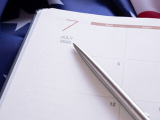 The pen point to July 2020 in a diary, put on American flag background. .