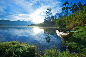Naklejka na ściany i meble Beautiful scenic background of boat and lake surrounded by mountains and forest with morning blue sky on background in hill country of Sri Lanka. Morning Sunrise to lake in upcountry, Sri Lanka.