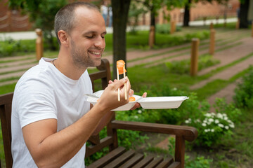 Young man sitting outside eating takeaway sushi