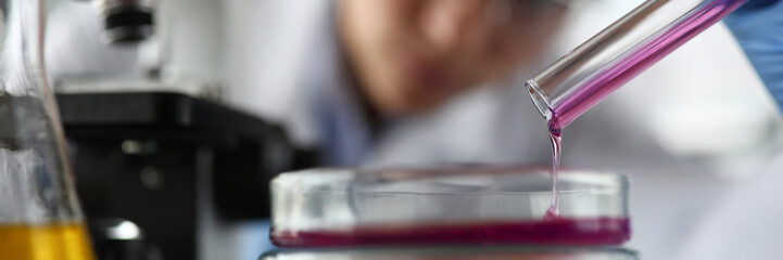 Close-up of laboratory assistant pouring reagent in test container. Researcher investigating liquid under microscope in research lab. Science experiments concept